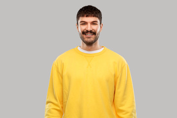 people concept - smiling young man in yellow sweatshirt over grey background