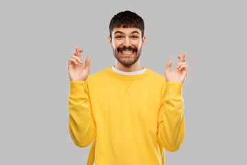 Fototapeta premium gesture, luck and people concept - smiling young man with crossed fingers in yellow sweatshirt over grey background