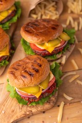 Home or restaurant cuisine. Two fresh large hamburgers with french fries on a wooden background. Vertical photo. Cafe and eateries, restaurant food.