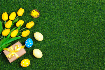 Easter eggs and yellow tulips on a green grass background.