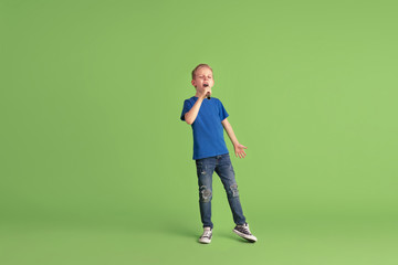 Fototapeta na wymiar Singing. Happy boy playing and having fun on green studio background. Caucasian kid in bright cloth looks playful, laughting, smiling. Concept of education, childhood, emotions, facial expression.