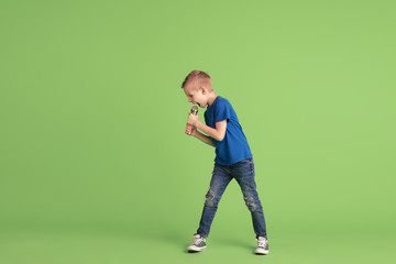 Fototapeta na wymiar Singing. Happy boy playing and having fun on green studio background. Caucasian kid in bright cloth looks playful, laughting, smiling. Concept of education, childhood, emotions, facial expression.