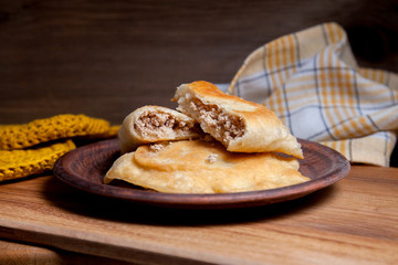 Clay plate of fried meat pies on wooden table.