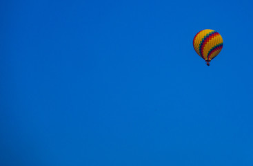 Hot air balloon, in yellow and some other color stripe, in the bright blue sky.  Can be used as background and copy space.