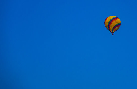 Hot air balloon, in yellow and some other color stripe, in the bright blue sky.  Can be used as background and copy space.