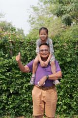 Relations and people concept. happy granddaughter sitting on grandfather's shoulders in a park.