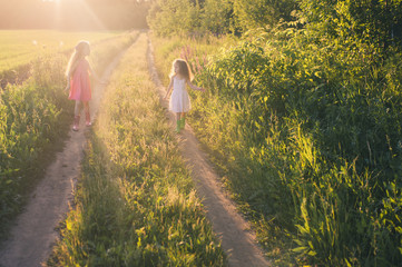 Two cute girls walking on a country road in a field at sunset