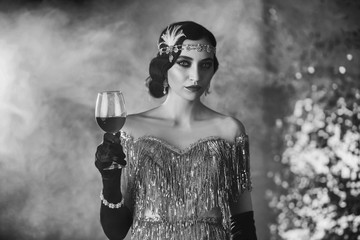 Black and white closeup portrait stylish retro woman in shine silver dress with glass of wine in...