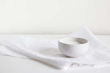 A salt shaker filled with white salt lies on a light towel on a gray background.