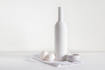 A white bottle of wine on a light background stands with a salt shaker and eggs on a towel.