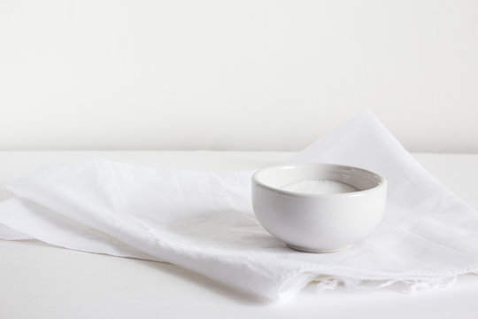 A salt shaker filled with white salt lies on a light towel on a gray background.