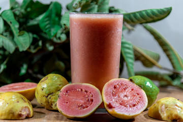 Glass of guava juice around fresh fruits and guava leaves in the background