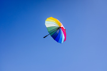 Multicolored umbrella flying suspended over bright blue sky background , with copy space.
