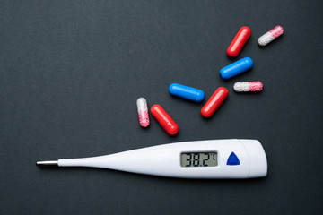 Fototapeta na wymiar Thermometer and medication on a black background. Treatment of a coronavirus, flu , or cold. Medical concep