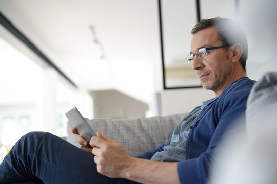 Middle-aged guy at home sitting in sofa with tablet