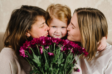 Portrait mother with flowers, grandmother kissing and hugging granddaughter and spend time together. International Women's Day. Happy Mother's Day. Holiday concept. Three generations of women.