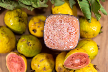 Glass of guava juice around fresh fruits and guava leaves