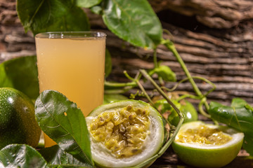 Glass of passion fruit juice among fresh broken fruits on a woody background