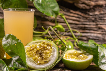 Glass of passion fruit juice among fresh broken fruits on a woody background