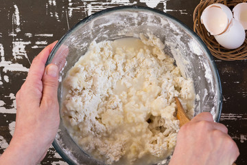 Woman hands mixing hot water and flour to make dough with wooden spoon on brown background