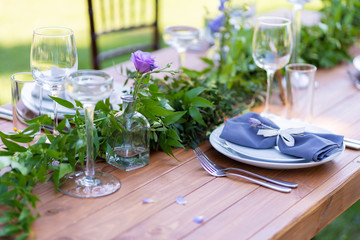A wooden table without a tablecloth is served and decorated with fresh flowers. Outdoor cafe