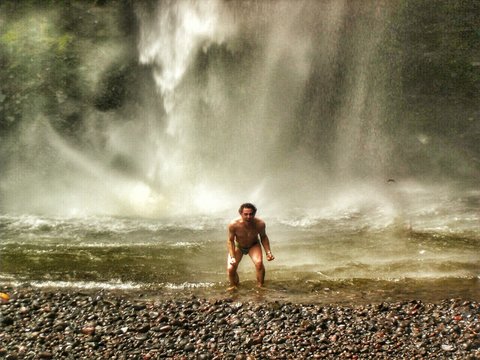 Man Screaming While Standing In Shallow Water Against Waterfall