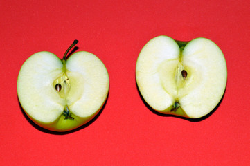 Two halves of a green juicy sliced ​​apple on red background