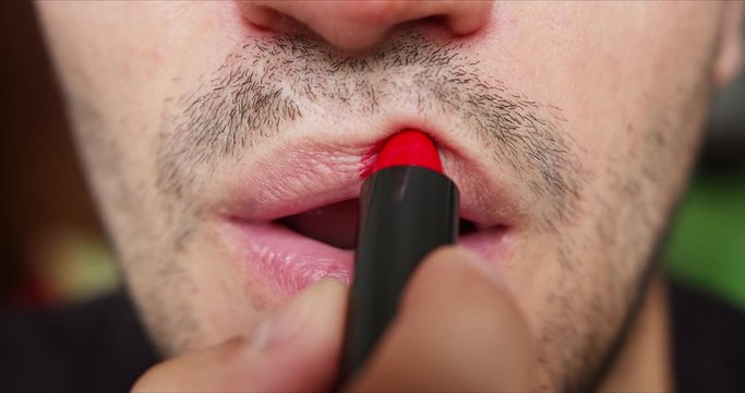 Closeup crop transgender guy with bristle applying red lipstick and smacking lips in slow motion