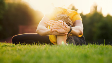 Young attractive woman practicing yoga in the park at sunset. Outdoor sport activity. Practice yoga...