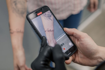 Tattoo artist recording a finished tattoo in a womans arm with his phone