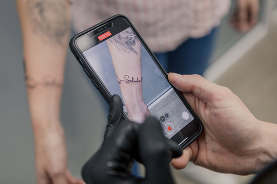 Tattoo Artist Recording A Finished Tattoo In A Womans Arm With His Phone