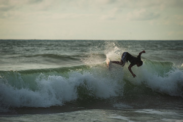 Young people ride on short boards, perform bright tricks on the waves during sunset.
