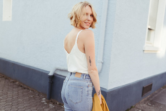 young woman with blonde short hair wearing a white top and jeans and smiling enjoying summertime