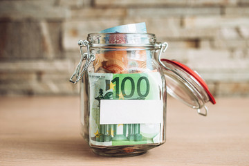 Banknotes of Euro in a glass jar and a place for signature - copyspace - piggy bank and stash