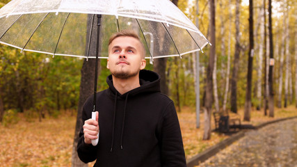 Portrait of a young man holding an umbrella walking along the autumn park in a rainy day