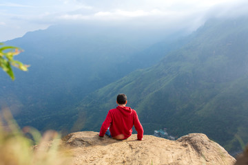 Naklejka premium A man enjoying the mountain scenery on the edge of a cliff
