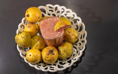 Guavas and glass of juice on white tray on marble table with dark background