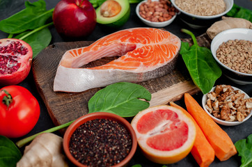 Selection of healthy food: salmon, fruits, seeds, cereals, superfoods, vegetables, leafy vegetables on a stone background. Healthy food for people.
