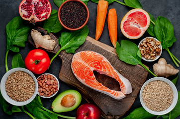 Selection of healthy food: salmon, fruits, seeds, cereals, superfoods, vegetables, leafy vegetables on a stone background. Healthy food for people.