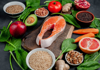 Selection of healthy food: salmon, fruits, seeds, cereals, superfoods, vegetables, leafy vegetables on a stone background. Healthy food for people.