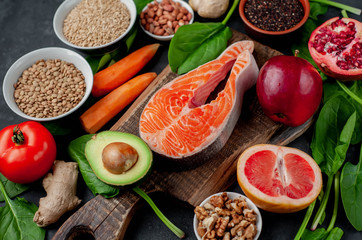Selection of healthy food: salmon, fruits, seeds, cereals, superfoods, vegetables, leafy vegetables on a stone background. Healthy food for people.