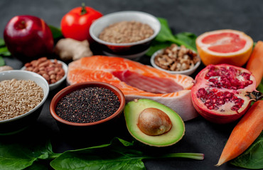 Selection of healthy food: salmon, fruits, seeds, cereals, superfoods, vegetables, leafy vegetables on a stone background. Healthy food for people.