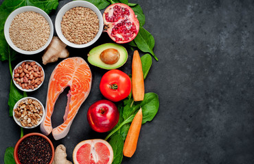 Selection of healthy food: salmon, fruits, seeds, cereals, superfoods, vegetables, leafy vegetables on a stone background  with copy space for your text. Healthy food for people.
