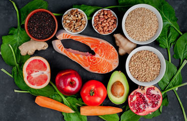 Selection of healthy food: salmon, fruits, seeds, cereals, superfoods, vegetables, leafy vegetables on a stone background. Healthy food for people.
