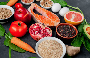 Selection of healthy food: salmon, fruits, seeds, cereals, superfoods, vegetables, leafy vegetables on a stone background. Healthy food for people.