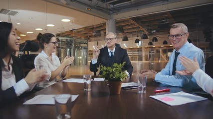 Business team clapping in celebration of a successful boardroom meeting.