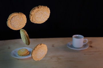 amaranth cookies floating in the air with black background and in the background a cup of coffee
