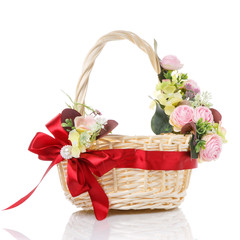 Fototapeta na wymiar Pink flowers wicker basket decorated with red ribbon bow on white background