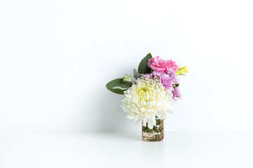 Beautiful floral arrangement of pink, purple and white flowers, in small glass vase on white table with a white background.
