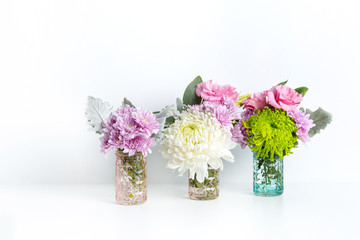 Colourful pastel flowers of pinks, purples and greens, in glass vases on a white table with a white background.	
